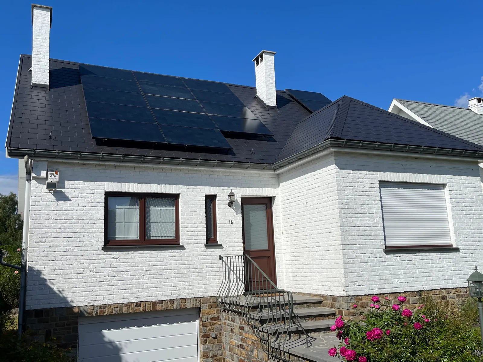 Maison à façade blanche avec toiture sombre et panneaux solaires